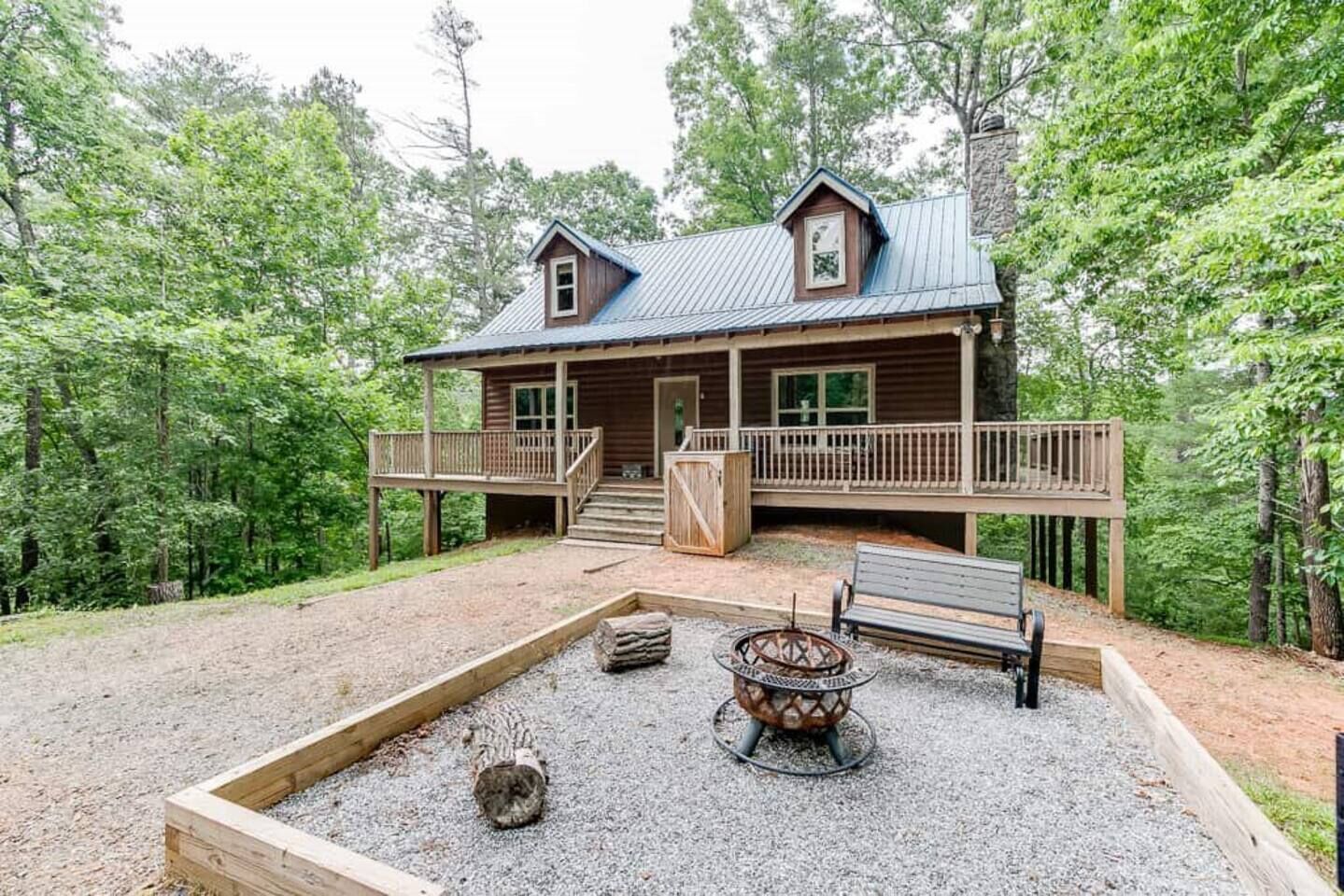 A wooden cabin with a deck, a fire pit, and a bench.