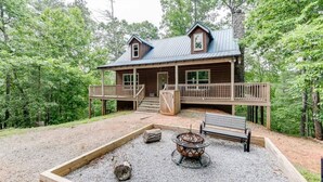A wooden cabin with a deck, a fire pit, and a bench.