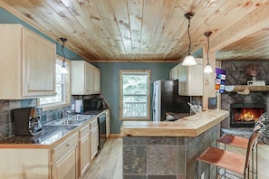 Enjoy cooking in this well-equipped kitchen with a stone fireplace, refrigerator, microwave, and coffee maker.