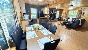 A dining area with a wooden table set for four, black chairs, and a view of the outdoors through large windows. - Listen to the River Sounds| Near Helen w Hot tub (Cleveland)