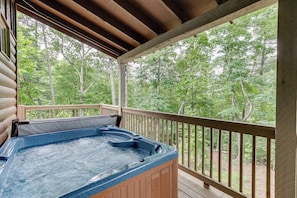 Relax in a hot tub on a raised deck overlooking a forest.