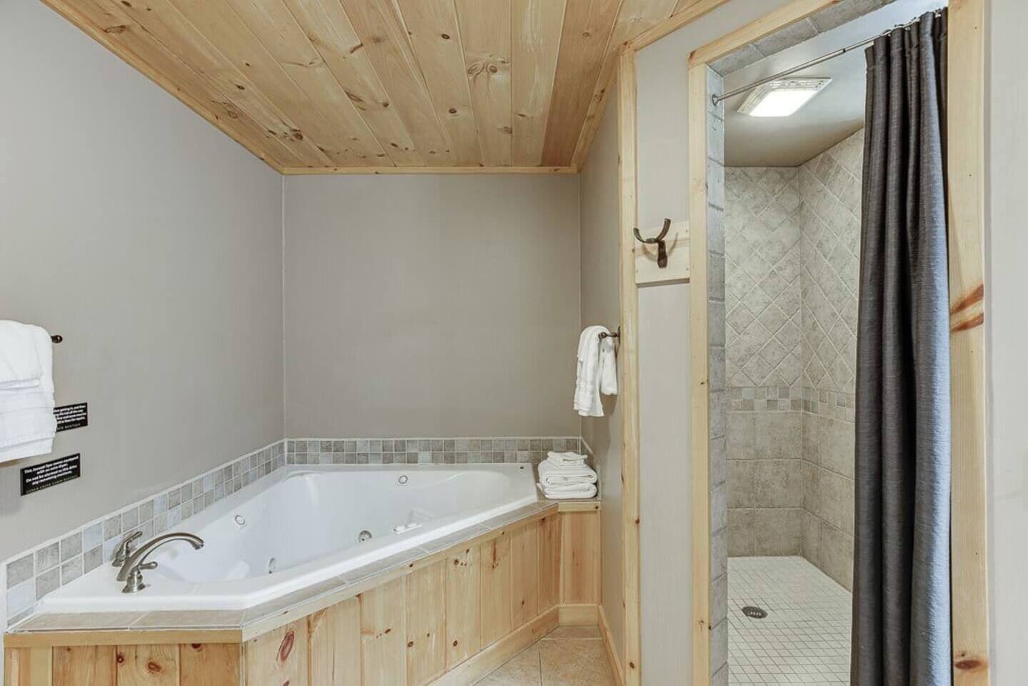 Ein Badezimmer mit Holzwandverkleidung, einer großen Badewanne, einer Duschkabine und einem Handtuchhalter.
