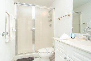 A bathroom with a glass shower enclosure, a toilet, a sink with toiletries, and a mirror. - Spacious condo on high floor with amazing bay & city views. WIFI + Parking (Sunny Isles Beach)