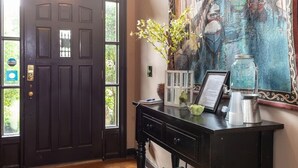 A dark wooden door with a window, a desk with a vase of flowers, a framed menu, and a coffee pot.