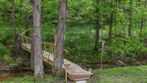 A wooden bridge over a stream in a forested area with a sign indicating a nature trail.