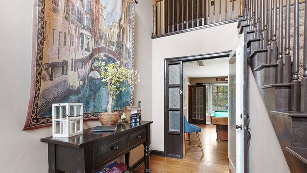 A hallway with a dark wooden console table, a large painting of a cityscape, and a staircase leading to an upper level.