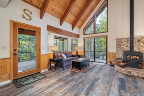 A spacious living room with a wooden ceiling, large windows, a stone fireplace, and a cozy seating area.