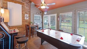 A pool table in a room with a brick wall, a ceiling fan, and a bar area with stools.