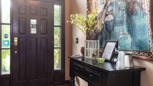 A dark wooden door with a window, a desk with a vase of flowers, a framed menu, and a decorative painting on the wall.