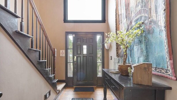 A hallway with a wooden staircase, a dark door, a rug, a bench, and a tapestry.