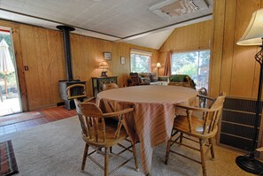 Ein gemütlicher Raum mit einem großen runden Tisch, Holzstühlen, einem Kamin und einem Fenster mit Blick.