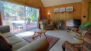 A living room with a sofa, armchair, and a television. There is a sliding glass door leading to an outdoor area.