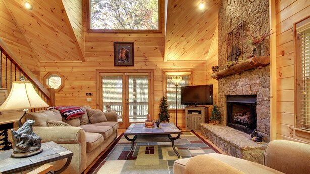 L’intérieur d’un chalet confortable, avec une cheminée, des murs en bois, un coin salon accueillant et un téléviseur.