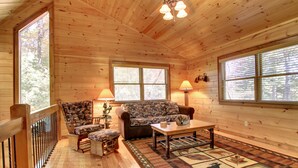 L’intérieur d’un chalet accueillant, avec des murs en bois, un canapé, deux fauteuils, une table basse et un tapis à motifs.