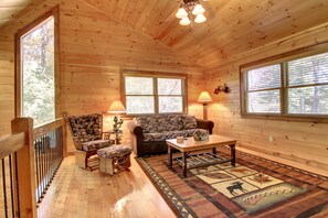 A cozy cabin interior with wooden walls, a sofa, two armchairs, a coffee table, and a patterned rug.