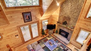 L’intérieur d’un chalet accueillant, avec une cheminée en pierre, des murs en bois, un téléviseur et une grande fenêtre.