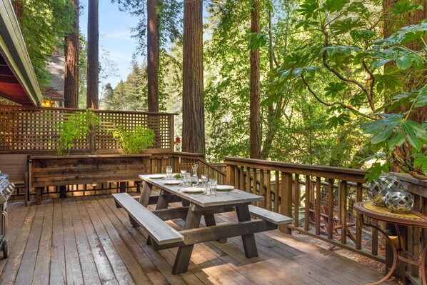 A wooden deck with picnic tables and benches, surrounded by tall trees and a wooden fence.