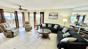 Un salon spacieux avec un grand canapé, deux fauteuils, une table basse et une vue sur l’océan grâce à de grandes fenêtres.