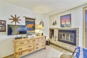 A living room with a fireplace, a television, a wooden dresser, and wall art.