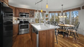 A kitchen with wooden cabinets, stainless steel appliances, a large island with a sink, and a dining area with a wooden table and chairs. - Cabin w/ Views, Jacuzzi Bathtub, Fireplace, Screened Porch, Outdoor Hot Tub (Ferguson)