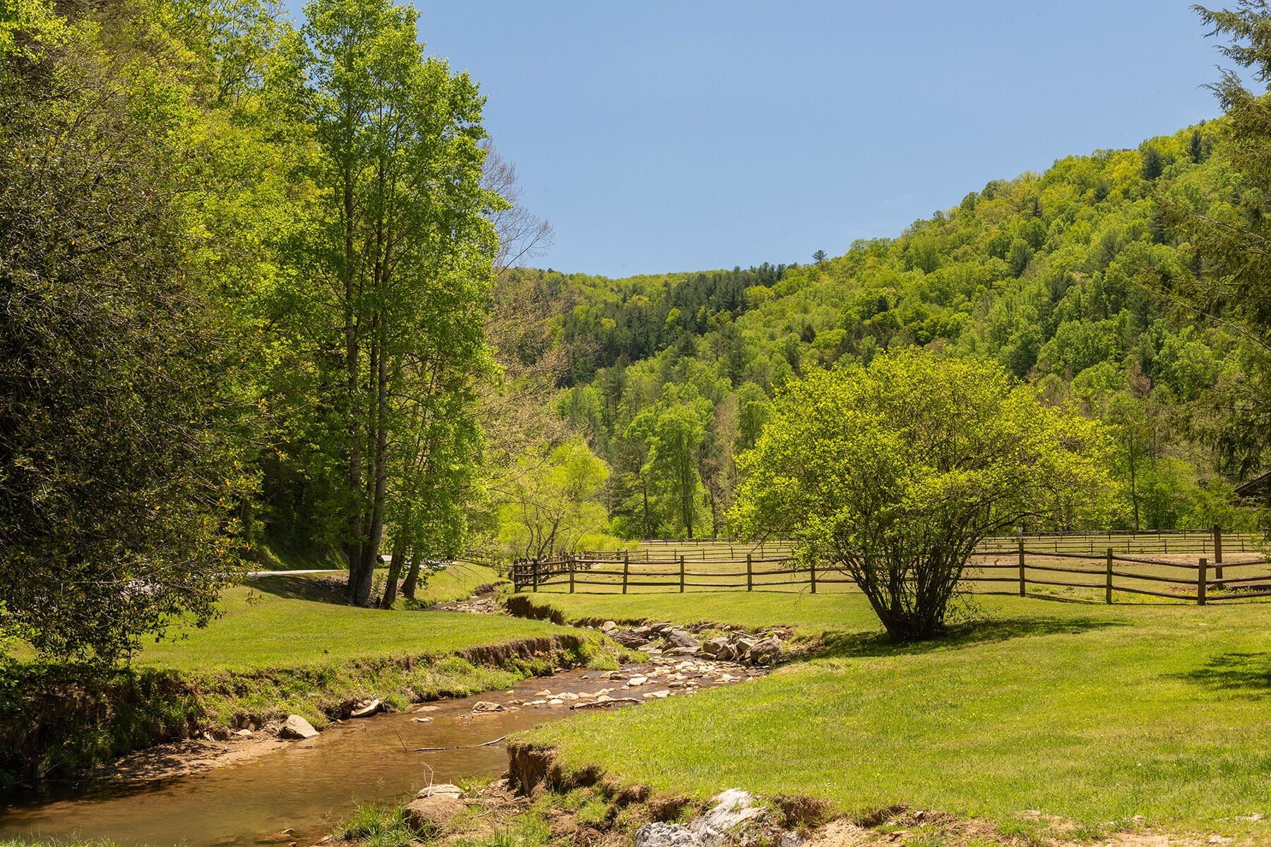 A rural landscape with a stream, grassy fields, and a wooden fence.