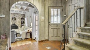A cozy living room with a fireplace, a sofa, and a coffee table. There is a staircase with a wooden railing leading to a door with a glass panel. - Villa Tranquila ~ Historic Mediterranean Home, Mountain Views, Spa! (Guerneville)