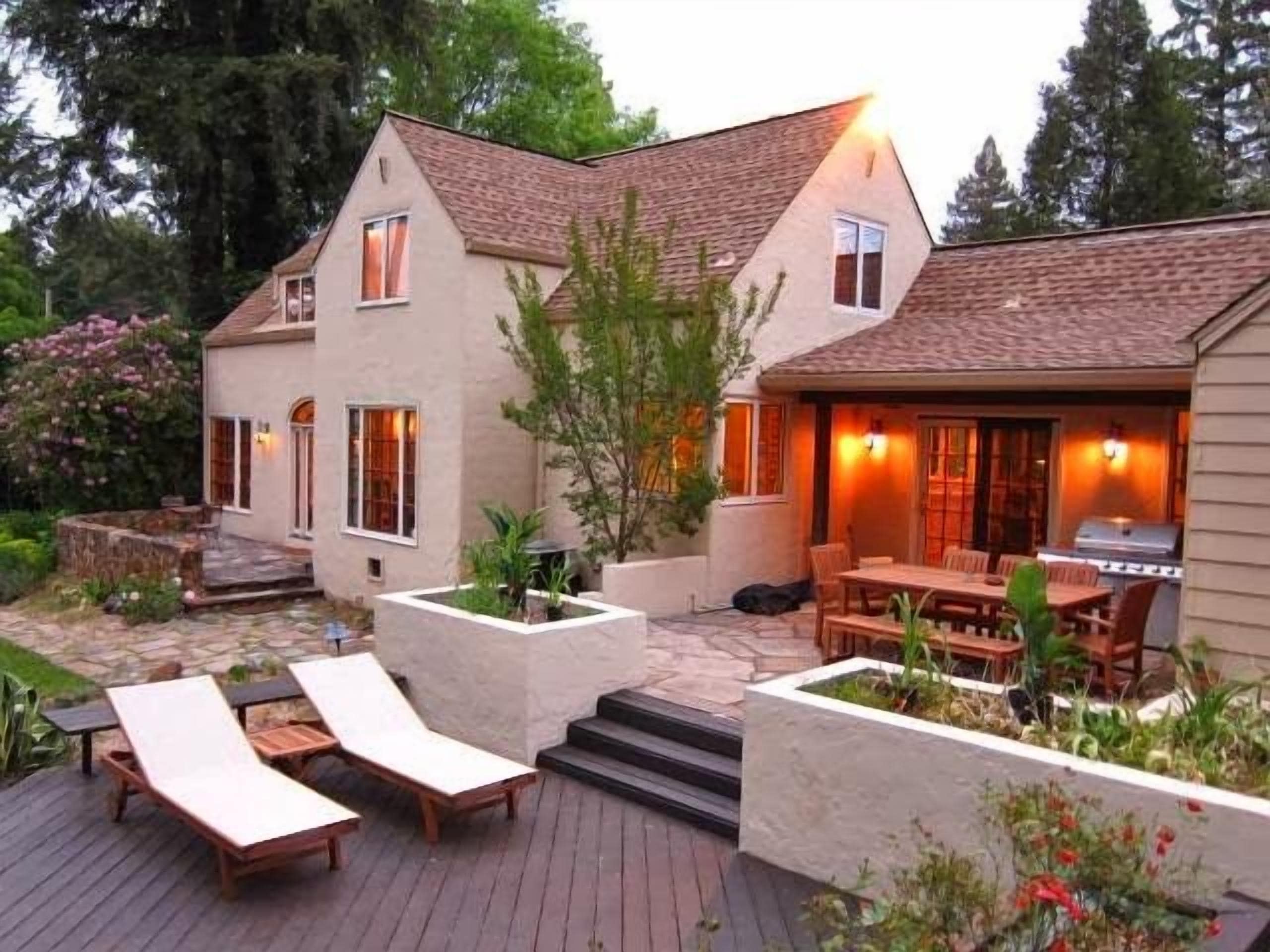 A two-story house with a patio area featuring lounge chairs and a barbecue grill.