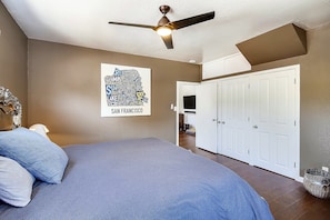 Une chambre à coucher comprenant un lit, un ventilateur de plafond, une œuvre d’art accrochée au mur et une armoire.