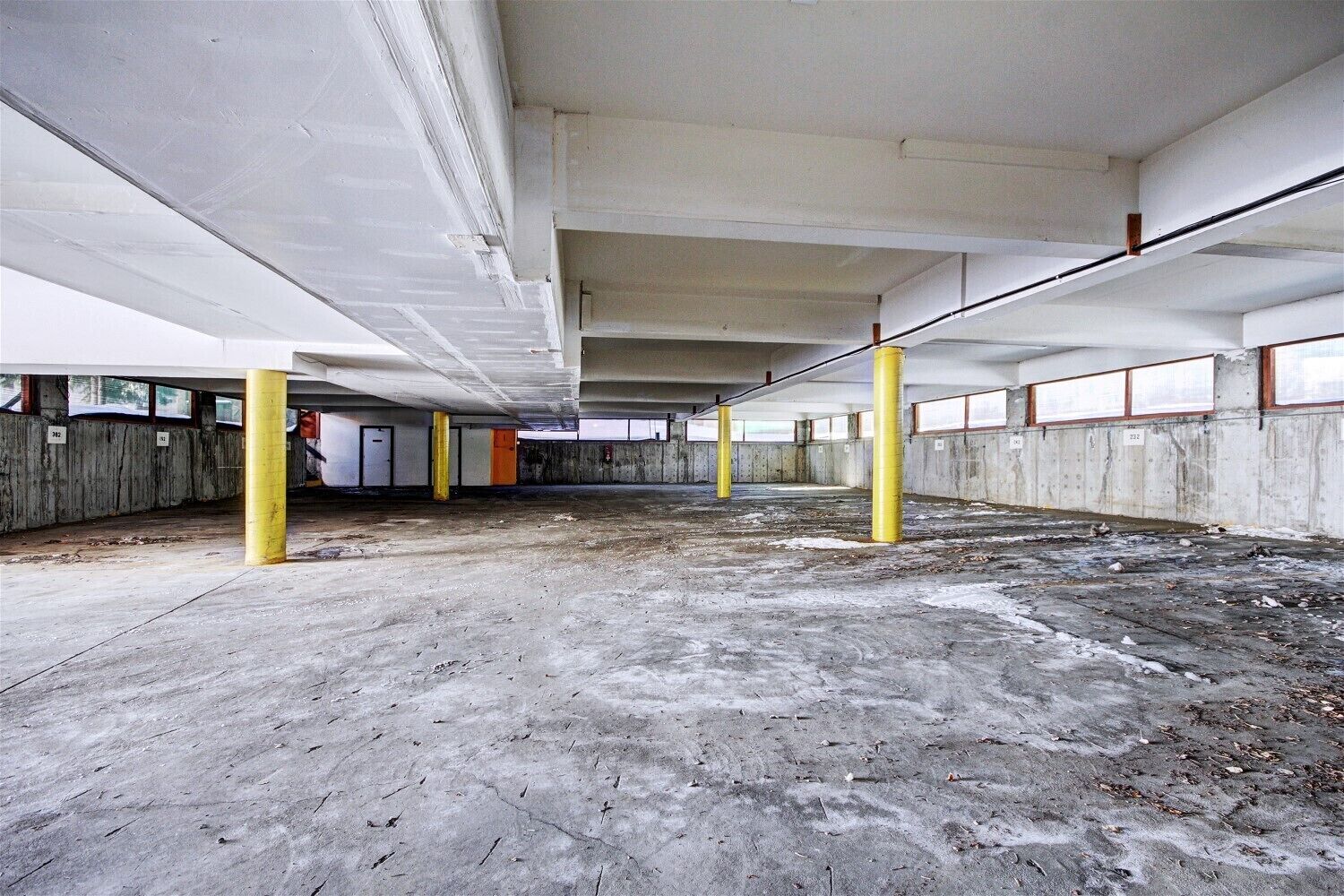 A large, empty parking garage with concrete floors and yellow pillars, featuring multiple levels and visible structural beams.