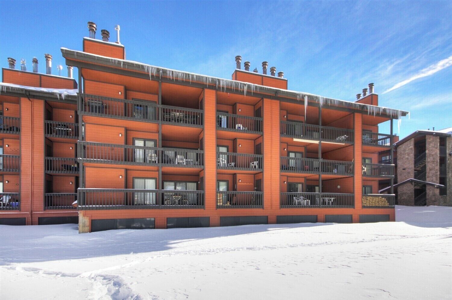A multi-story building with balconies, a snow-covered ground, and a clear sky.