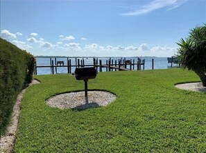 A well-maintained grassy area with a barbecue grill, a wooden dock extending into a body of water, and a clear sky.