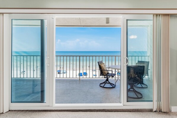A balcony with a view of the beach, a table, and two chairs.