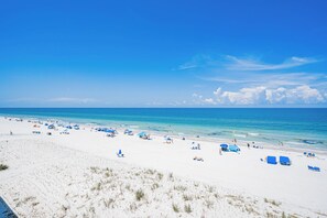 A beach with white sand, clear blue water, and a clear sky.