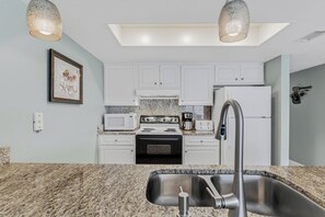 A kitchen with white cabinets, a granite countertop, a stainless steel sink, a microwave, a stove, and a refrigerator.