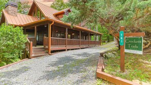 A cabin with a wooden porch, a stone chimney, and a gravel driveway.