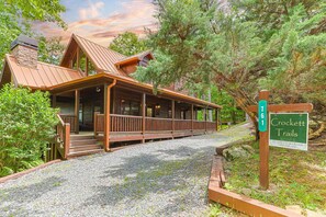 Une cabane dotée d’un porche en bois, d’une cheminée en pierre et d’une allée gravillonnée.