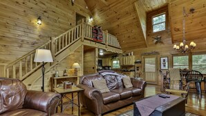 A wooden cabin interior with a staircase, leather furniture, a dining area, and a kitchen.