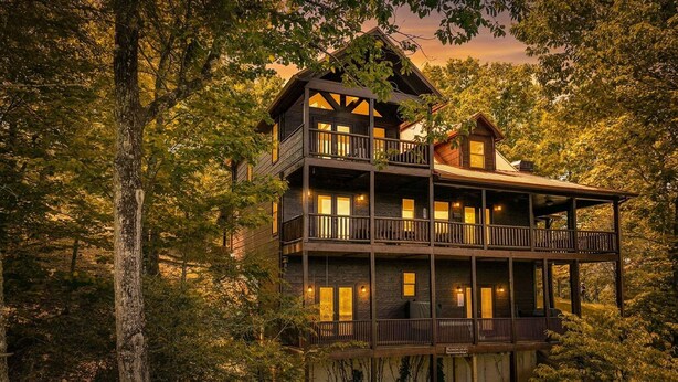 A multi-story log cabin with balconies, surrounded by dense forest.