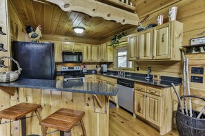Una cocina de estilo cabaña de madera con encimera de granito, armarios de madera, microondas, estufa, fregadero y lavavajillas.