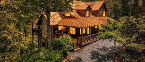 A cabin with a wooden exterior, a porch, and a gravel driveway surrounded by trees.