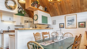 A cozy kitchen with white cabinets, a wooden dining table, and a green mat. - Chalet #6, Charming Cabin Perfect Location steps t (Mammoth Lakes)