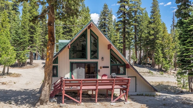 A cabin with a sloped roof, large windows, and a wooden deck with chairs. - Chalet #6, Charming Cabin Perfect Location steps t (Mammoth Lakes)