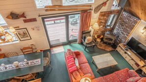 A cozy cabin interior with a fireplace, a dining area, and a large window overlooking a deck. - Chalet #6, Charming Cabin Perfect Location steps t (Mammoth Lakes)