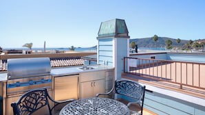 En udendørs terrasse med grill, siddepladser og havudsigt.
