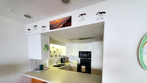A modern kitchen with white cabinets, a black microwave, and a large island with two orange stools.