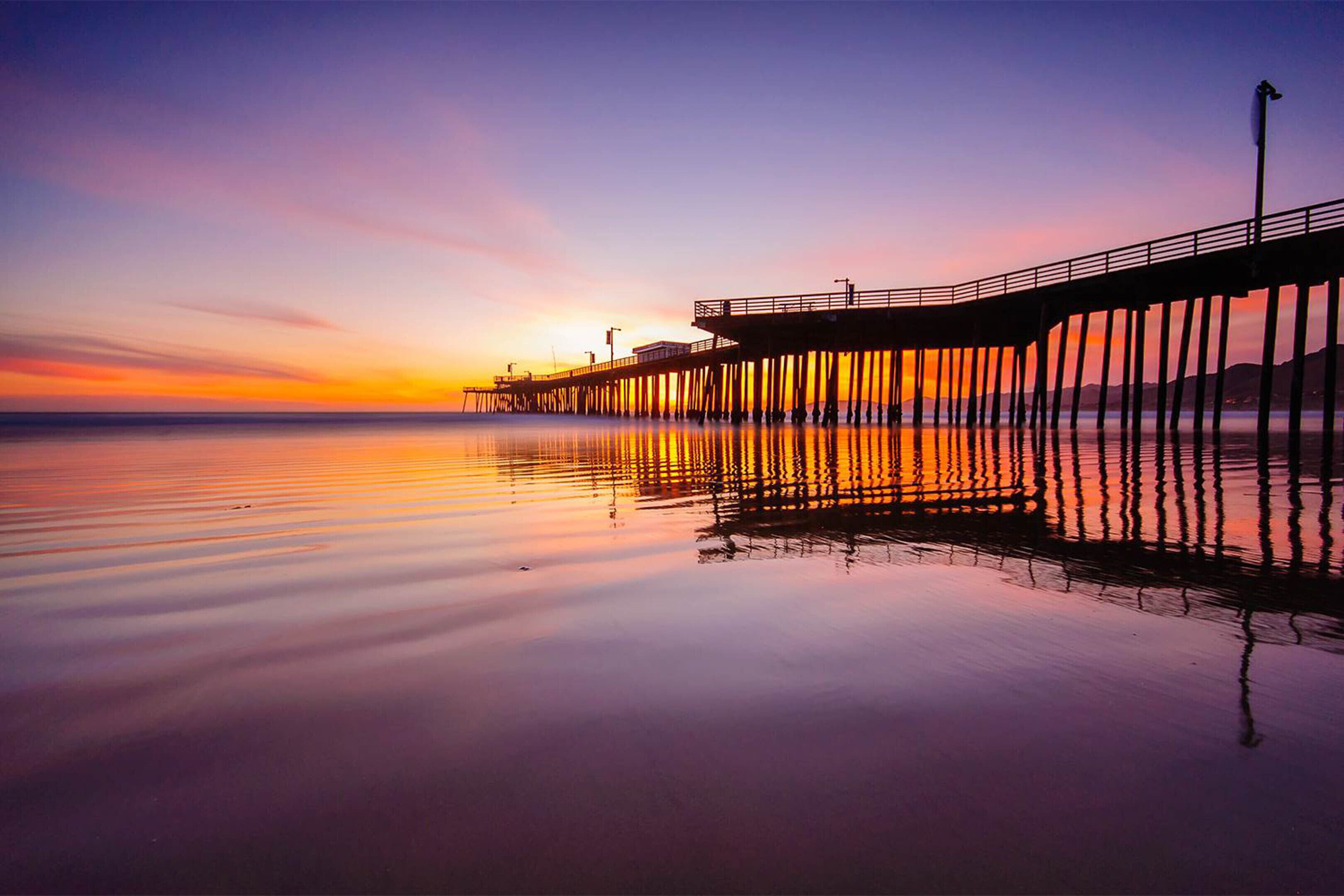 A pier extending into calm waters at sunset with a clear sky.