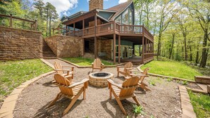 Une cabane avec un escalier en pierre menant à une terrasse, entourée d’un foyer et de chaises en bois.