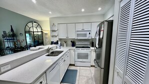 A modern kitchen with white cabinetry, a built-in oven, microwave, and refrigerator. - Beach chic Gold-rated condo overlooking quiet lagoon! (Saint Augustine)