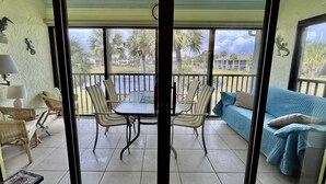 A balcony with a table and chairs, a sofa, and a view of palm trees and buildings. - Beach chic Gold-rated condo overlooking quiet lagoon! (Saint Augustine)