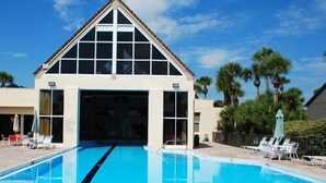 A hotel with a swimming pool, a covered entrance, and palm trees in the background. - Beach chic Gold-rated condo overlooking quiet lagoon! (Saint Augustine)